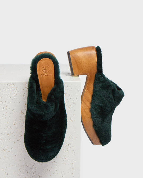 Dark green, plush fur clogs with a wooden sole and block heel, featuring a smooth, rounded toe and a branded insole.