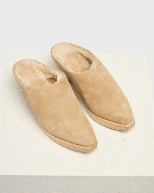 Beige suede slippers with a pointed toe, plush fur lining, and a flat sole, featuring a minimalist design and soft texture.