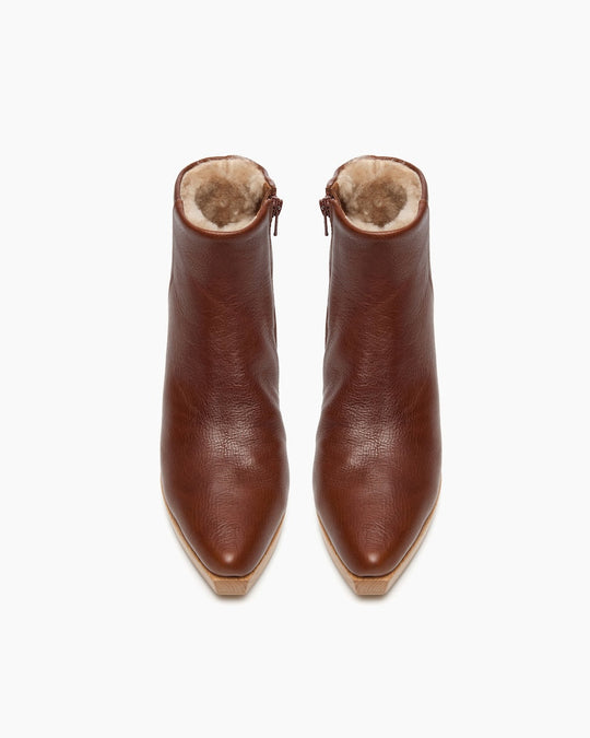 Brown leather ankle boots with a pointed toe, featuring a plush, fur-lined interior and side zippers, showcasing a smooth texture and a sleek, modern design.