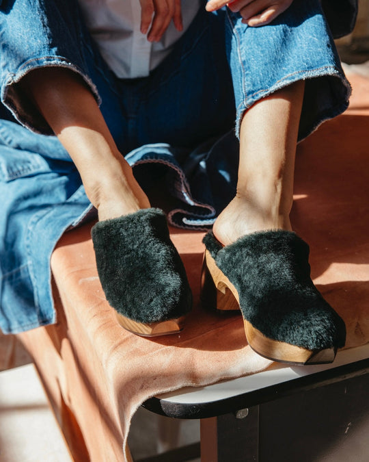 Hunter Green Shearling slip-on clogs with wooden soles worn by a person in blue denim pants.