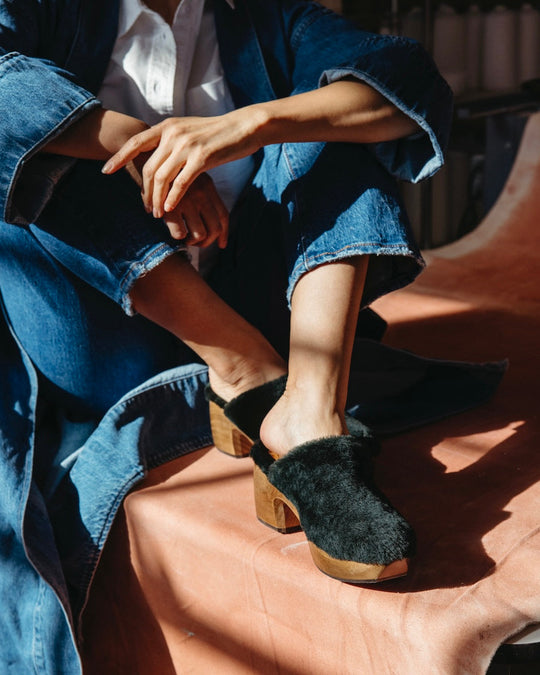 Hunter Green Shearling slip-on clogs with wooden block heels, worn by a person dressed in a denim outfit.