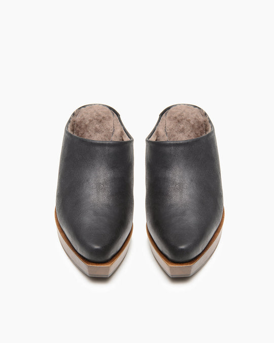 A pair of black leather slip-on shoes with a smooth texture, tapered toe, wooden sole, and a soft, fur-lined interior.