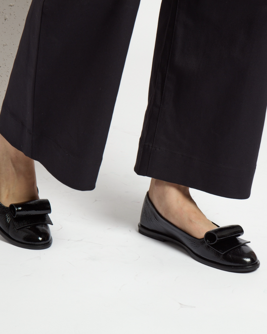 Black patent leather ballet flats with a glossy finish, featuring a distinctive large loop on the toe and a sleek, rounded shape.