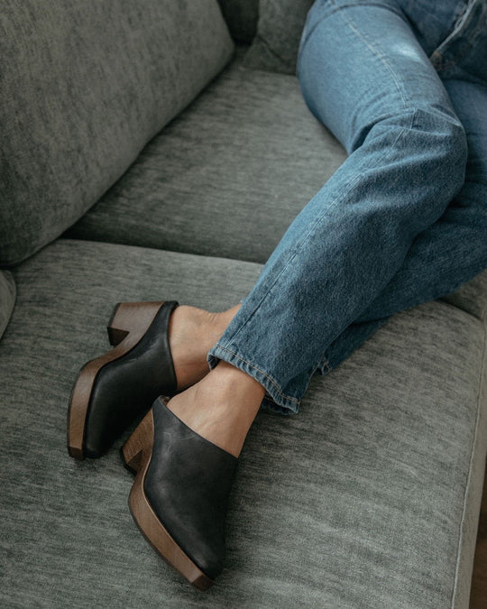 Women's legs and feet laying on a couch wearing jeans with the Kera Shearling Clog.